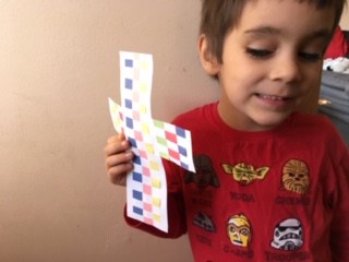 one kid holding a woven paper cross craft